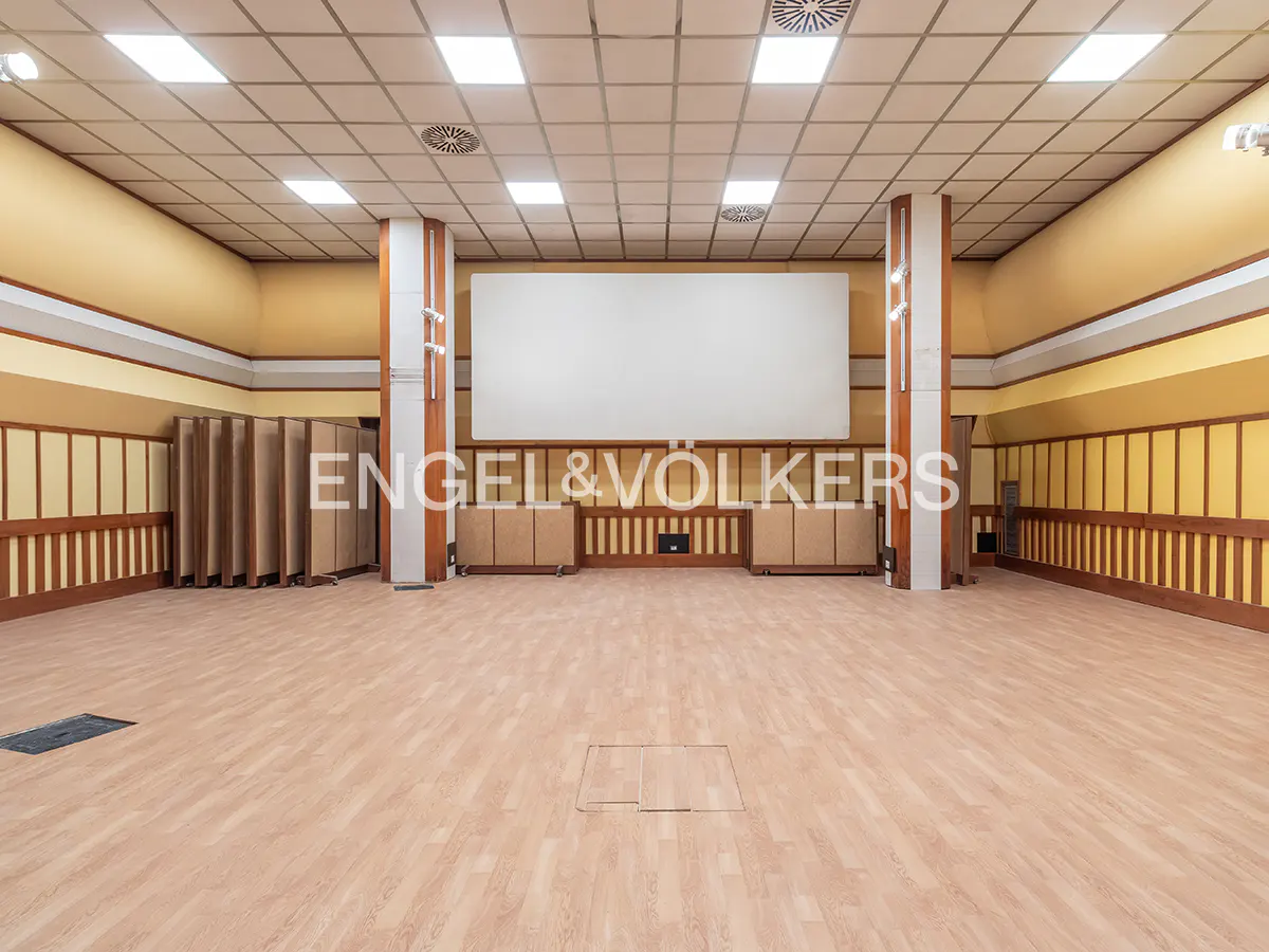 A spacious, empty conference room with light wood floors, yellow walls, wood paneling, and a large white projection screen.