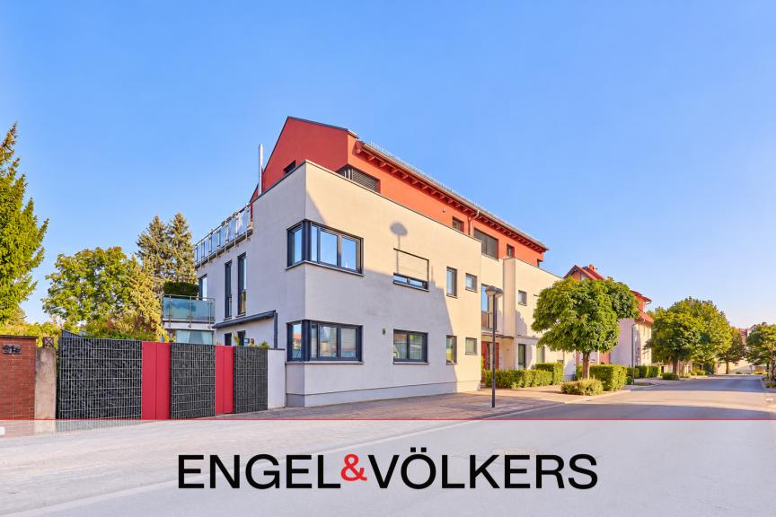 Modern white apartment building with a red roof and stone-filled fence under a clear blue sky. [AI-generated text]