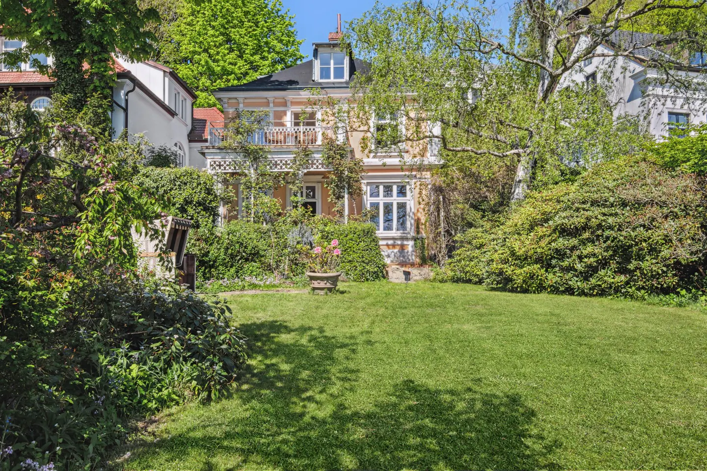 Two-story peach house with a black roof, white trim, and a green lawn surrounded by trees and bushes.