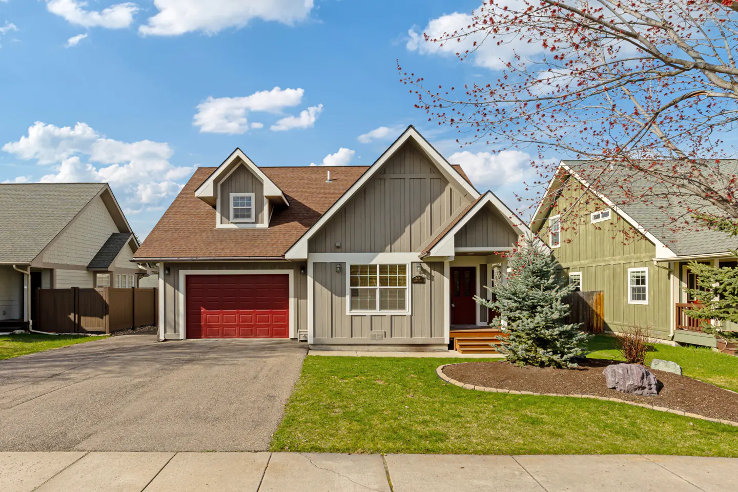 A single-family home with gray siding, a red garage door, and a brown roof on a sunny day.