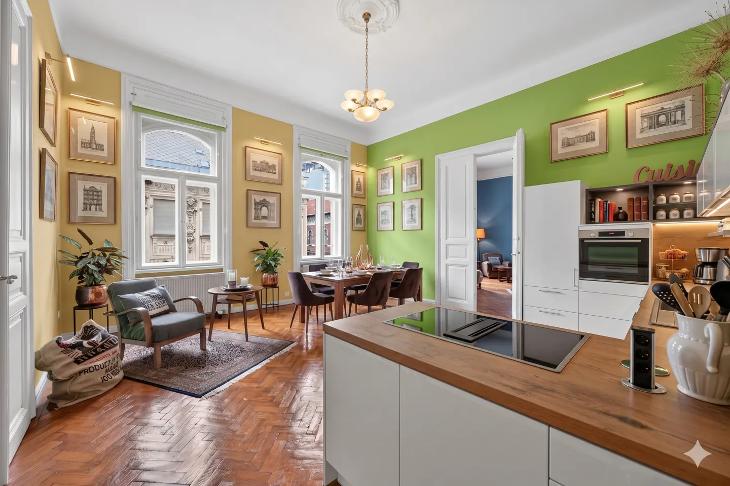 Bright, eclectic apartment with yellow and green walls, herringbone floors, and framed art. A dining table and modern kitchen are visible.