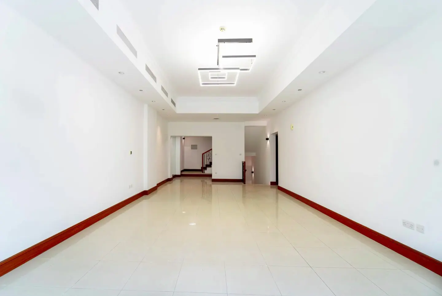Bright, empty room with white walls, tile floor, and dark wood trim. A modern light fixture hangs from the ceiling.