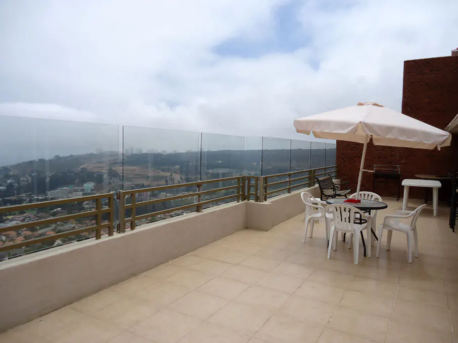 Outdoor patio with glass railing overlooking a city. White table and chairs under a large umbrella.