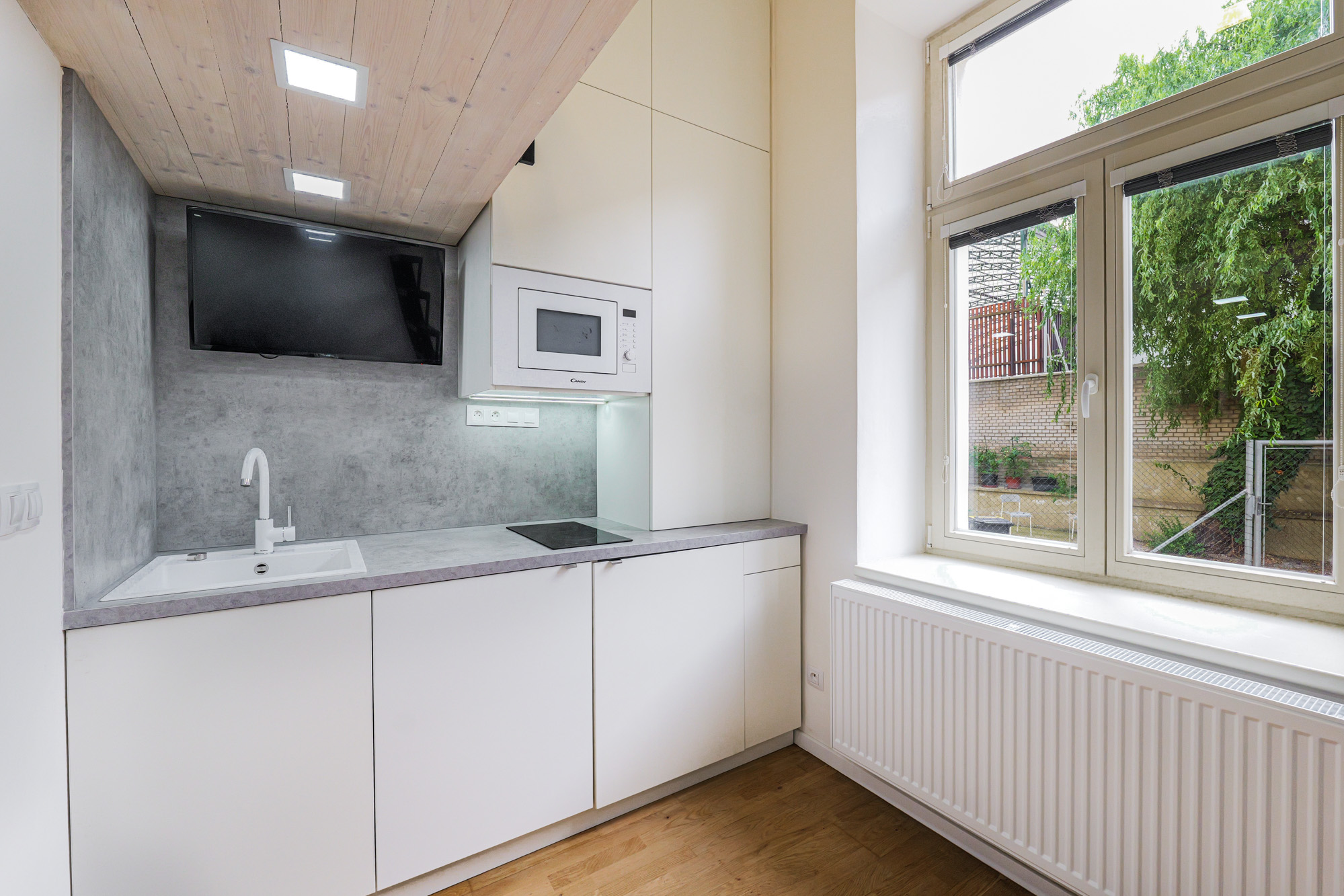 Modern kitchen with white cabinets, grey concrete backsplash, built-in microwave, and a large window overlooking a garden. [AI-generated text]