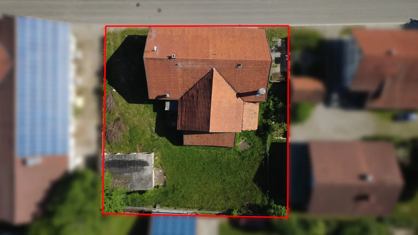 Aerial view of a house with a red tile roof, green lawn, and a red border.