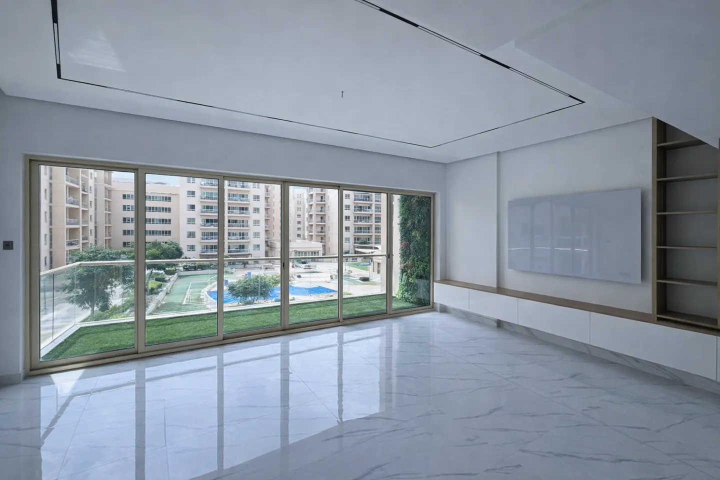 Bright, empty room with marble floors and a large window overlooking a courtyard with a pool and buildings. A white media console is on the right.