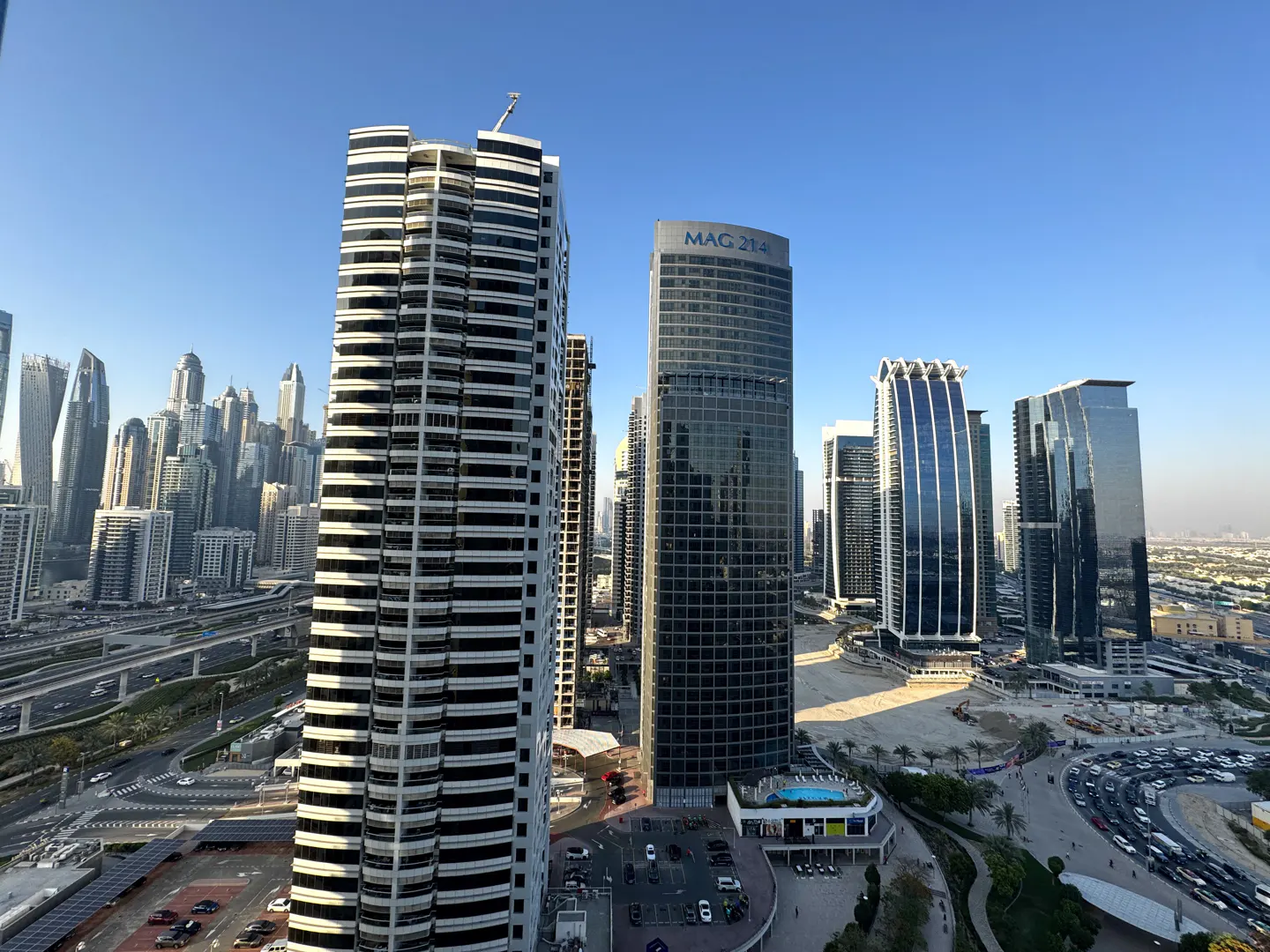 Cityscape view of Dubai with modern high-rise buildings under a clear blue sky. Traffic flows on roads below.