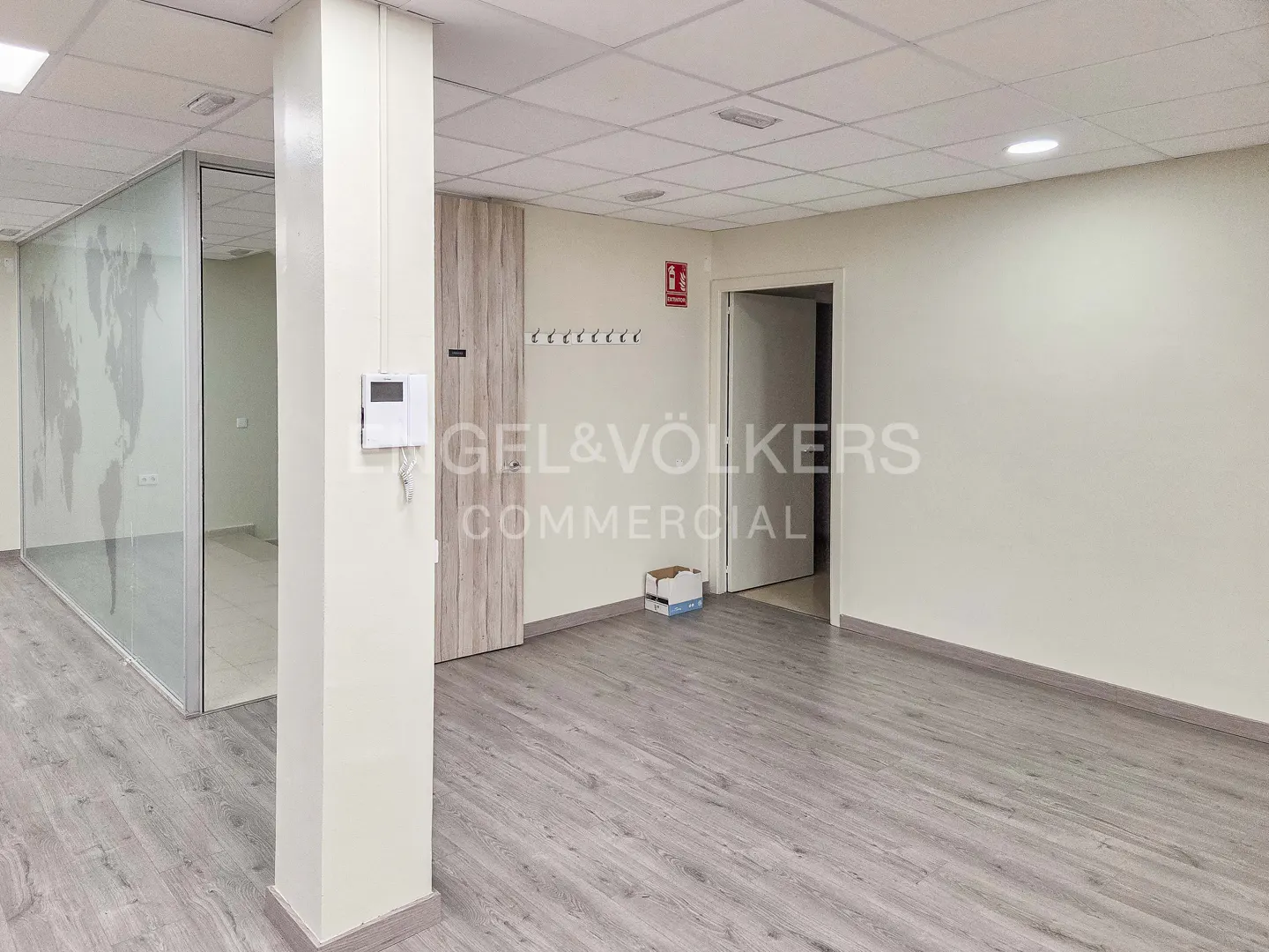 Bright, empty office space with gray wood-look floors, white walls, and a glass-walled room with a world map design.