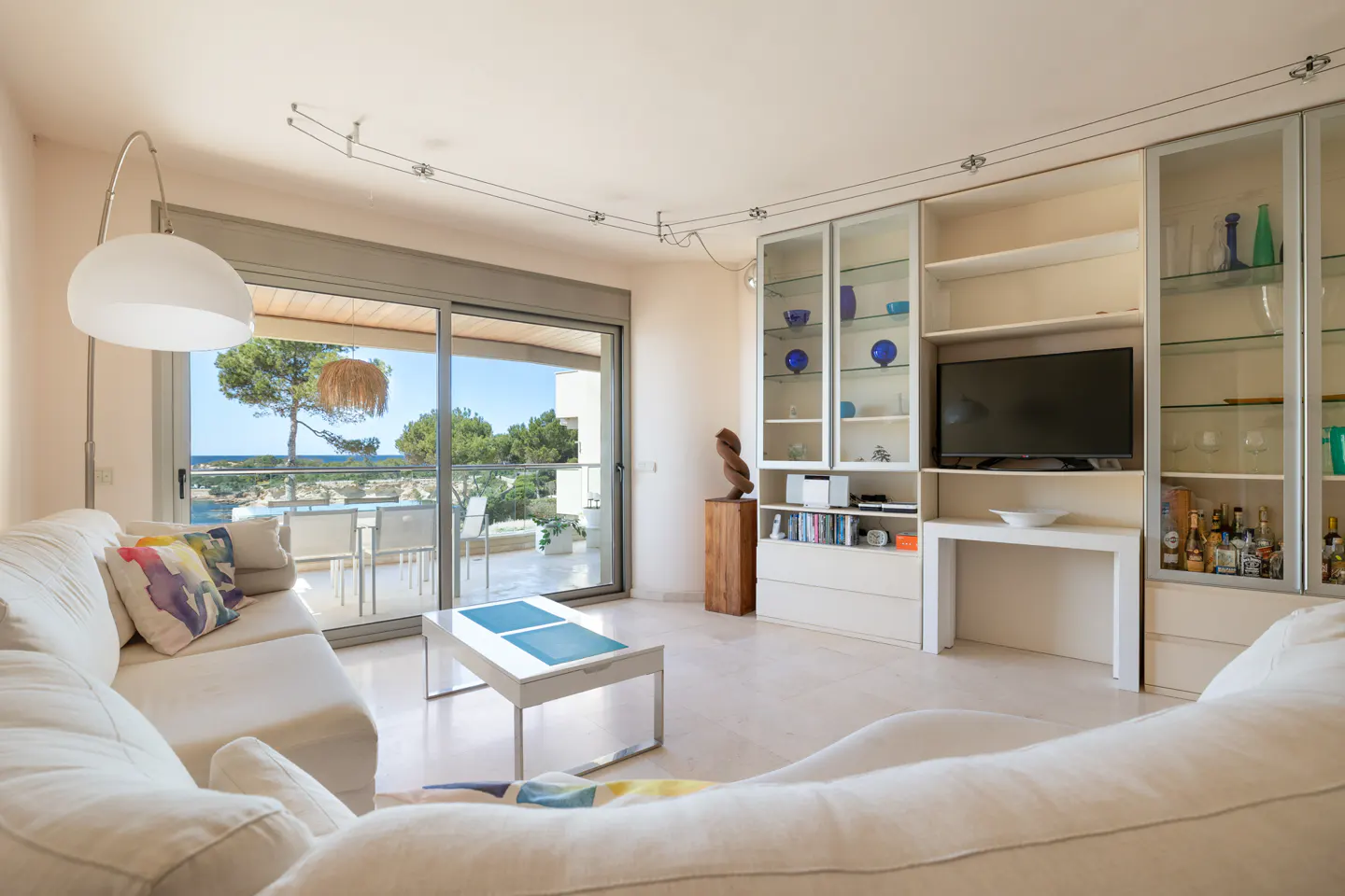 Bright living room with white sofas, a TV, and a balcony overlooking the ocean.
