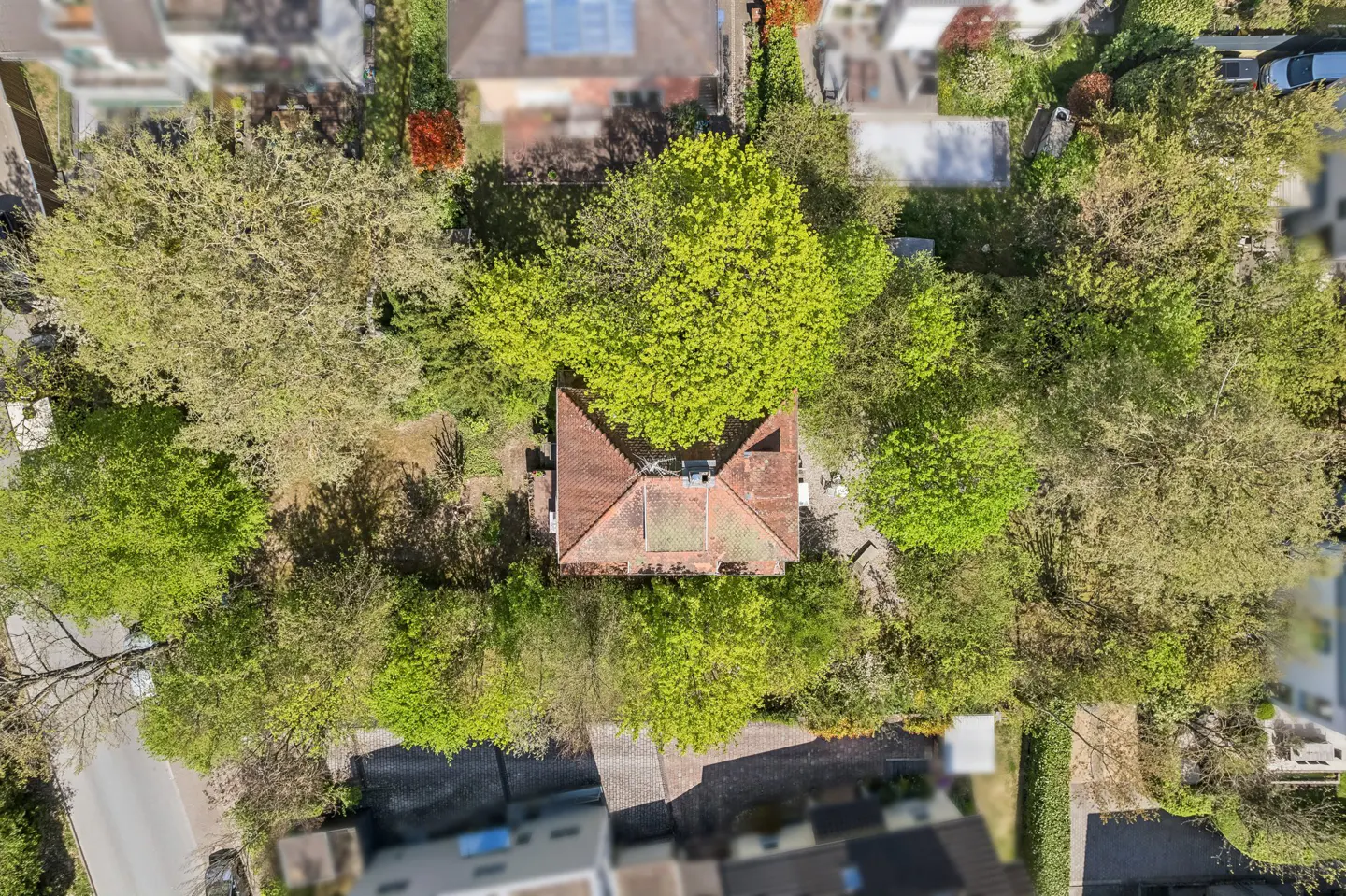 Aerial view of a house with a red tile roof, surrounded by lush green trees in a residential neighborhood.