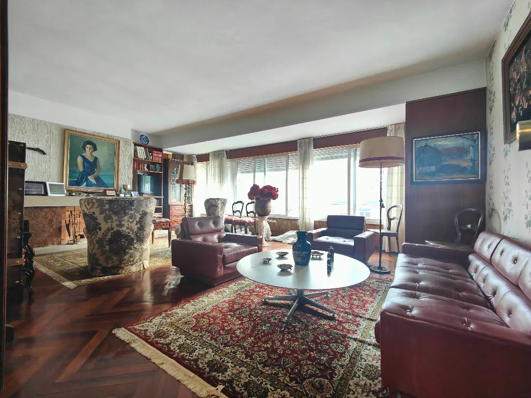 Wide shot of a living room with red leather furniture, a round white table, and a red patterned rug on a herringbone wood floor.