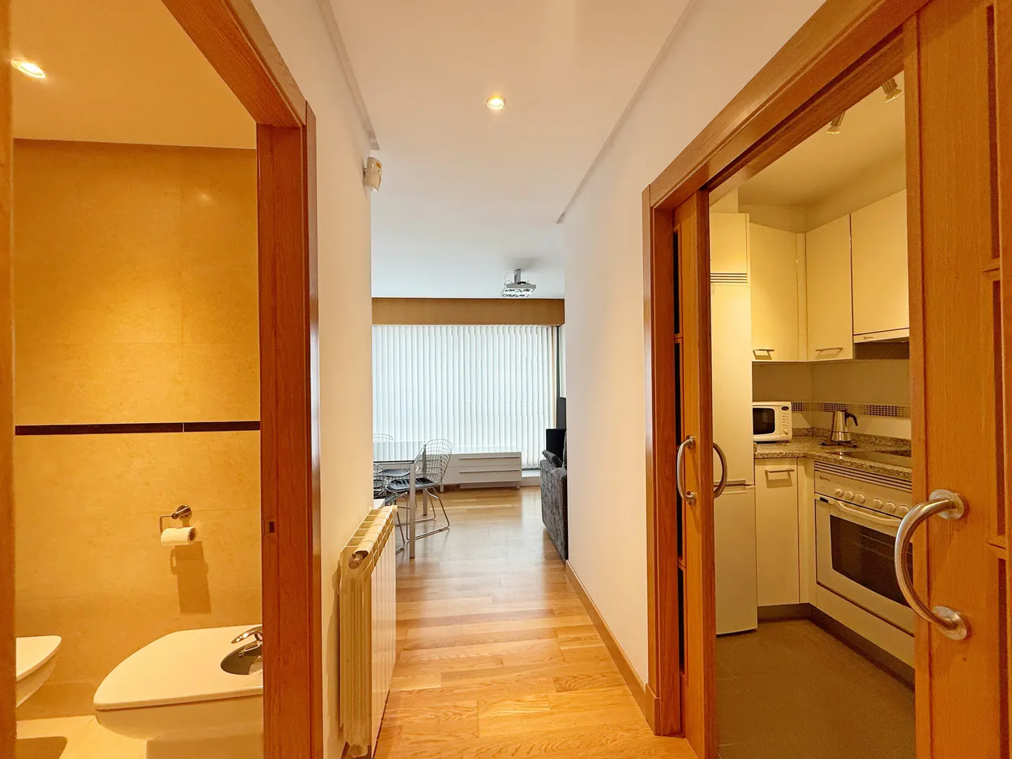 Hallway view with wood floors, bathroom on the left, kitchen on the right, and living room straight ahead.
