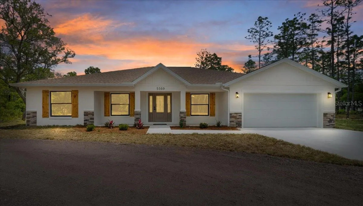 A single-story white house with a brown roof, shutters, and a two-car garage at sunset.