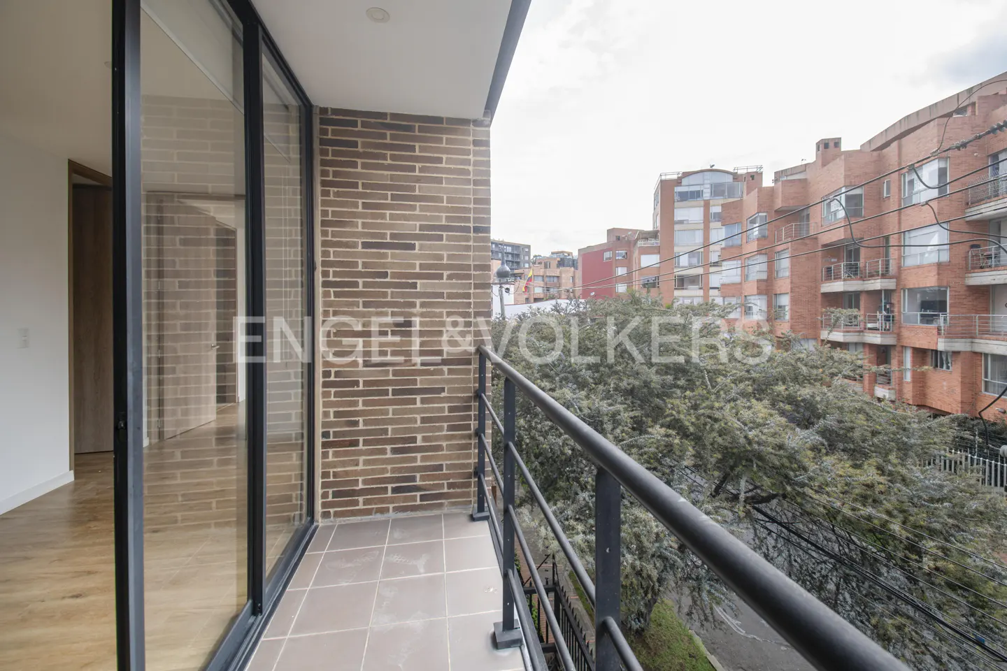 Balcony view with brick wall, black railing, and city buildings in the background. Engel & Volkers logo visible.