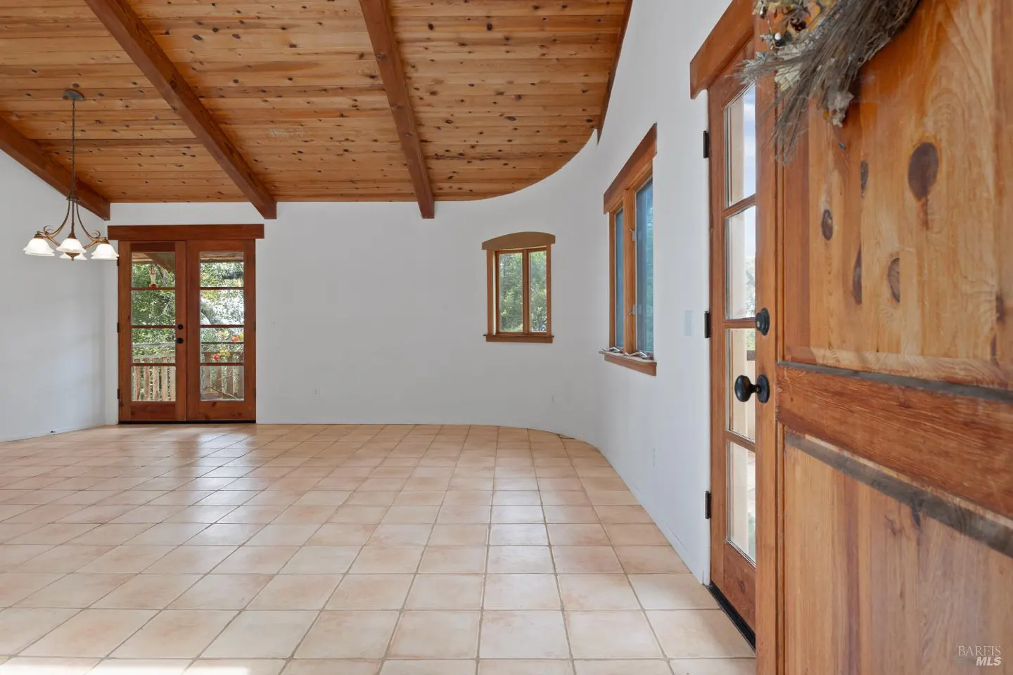 An interior view of a room with a wood ceiling, tile floor, and a wooden door with a wreath.