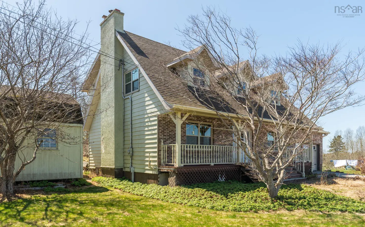 Exterior view of a light green two-story house with a brick porch and a brown shingled roof. A tall chimney is on the left side.