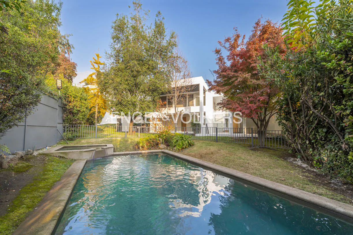 Backyard view of a modern white house with a pool, green lawn, and trees under a blue sky.
