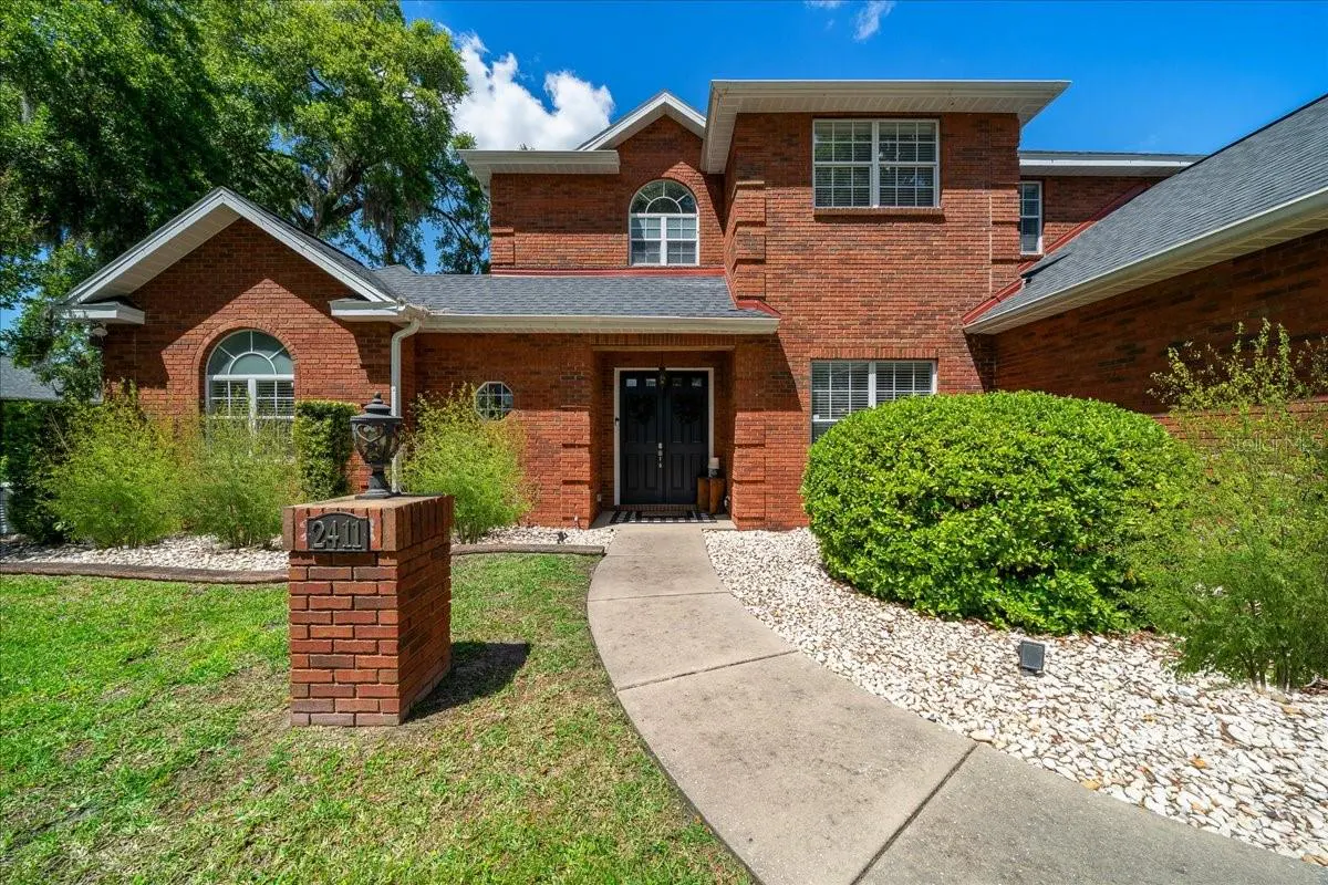 Two-story red brick house with a black front door, gray roof, and a concrete walkway leading to the entrance. A brick mailbox stands on the lawn.