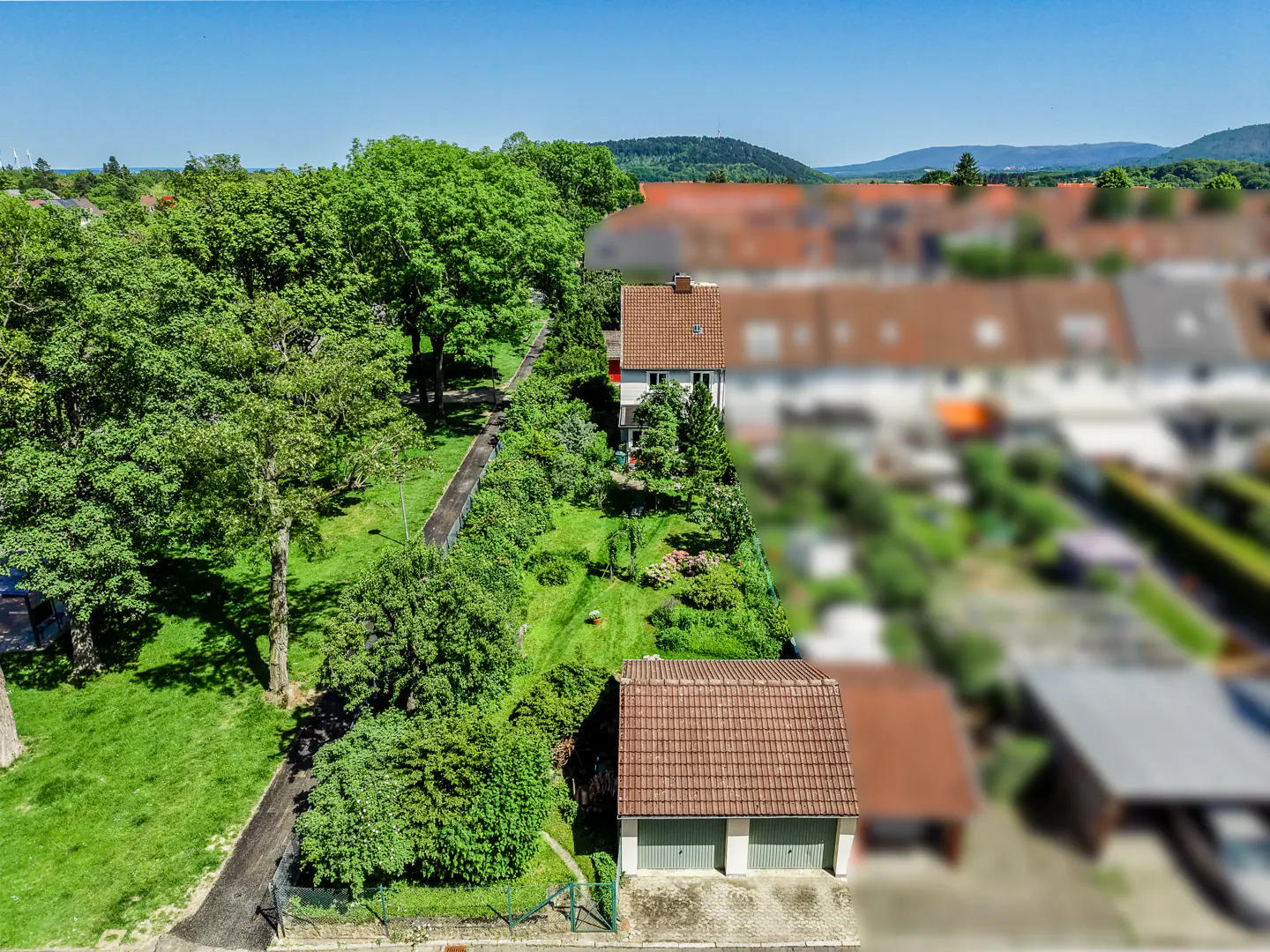 Aerial view of a house with a large green garden, mature trees, and a detached garage in a suburban neighborhood.