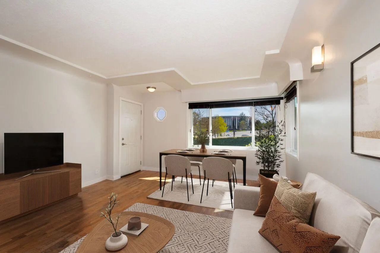 Bright living room with hardwood floors, white walls, and a dining table near a window with a view. A white sofa and TV are also visible.