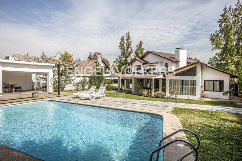 A wide shot of a white house with a pool and two white lounge chairs.
