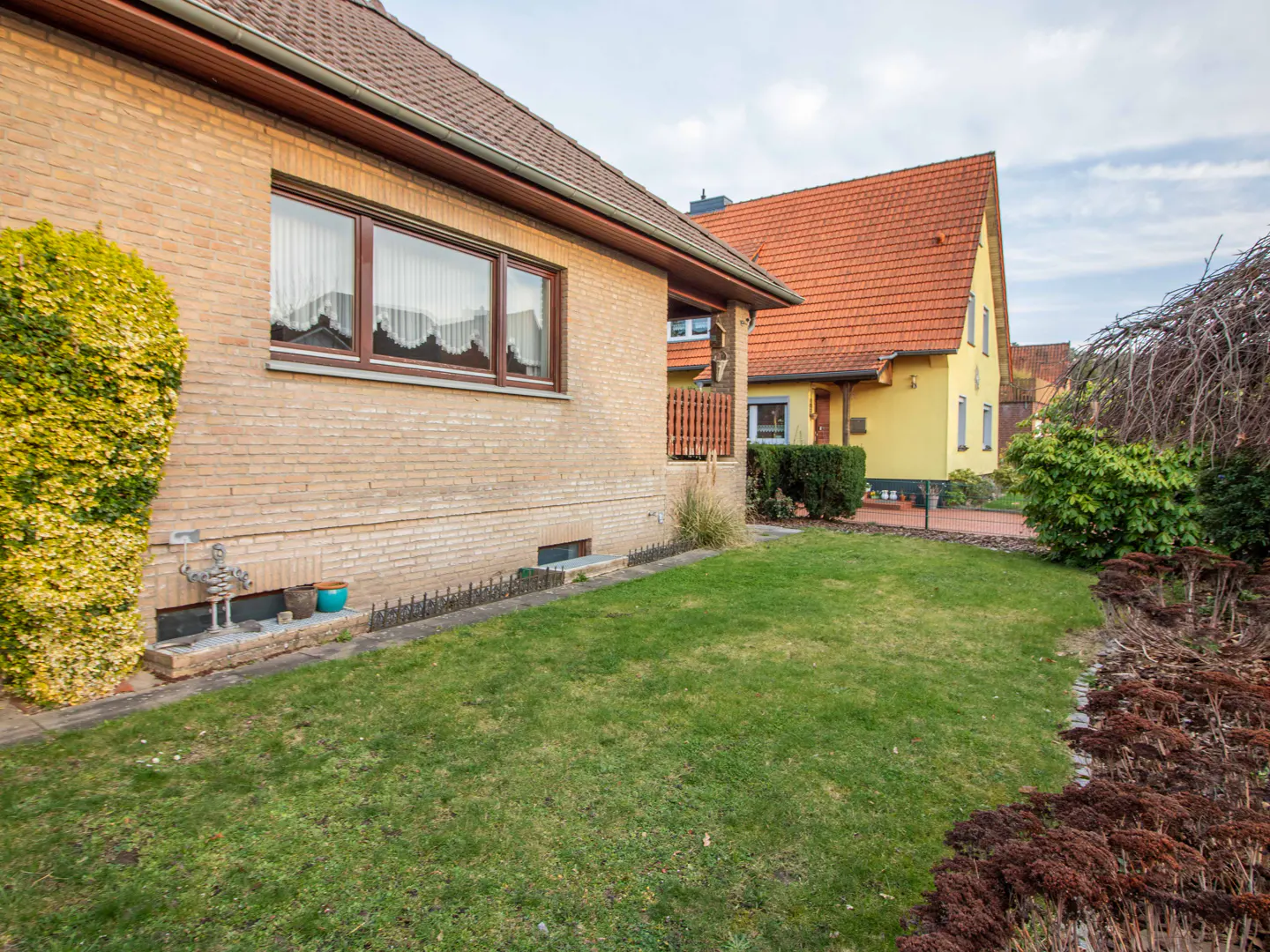 A tan brick house with brown trim and a green lawn. A yellow house with a red roof is in the background.