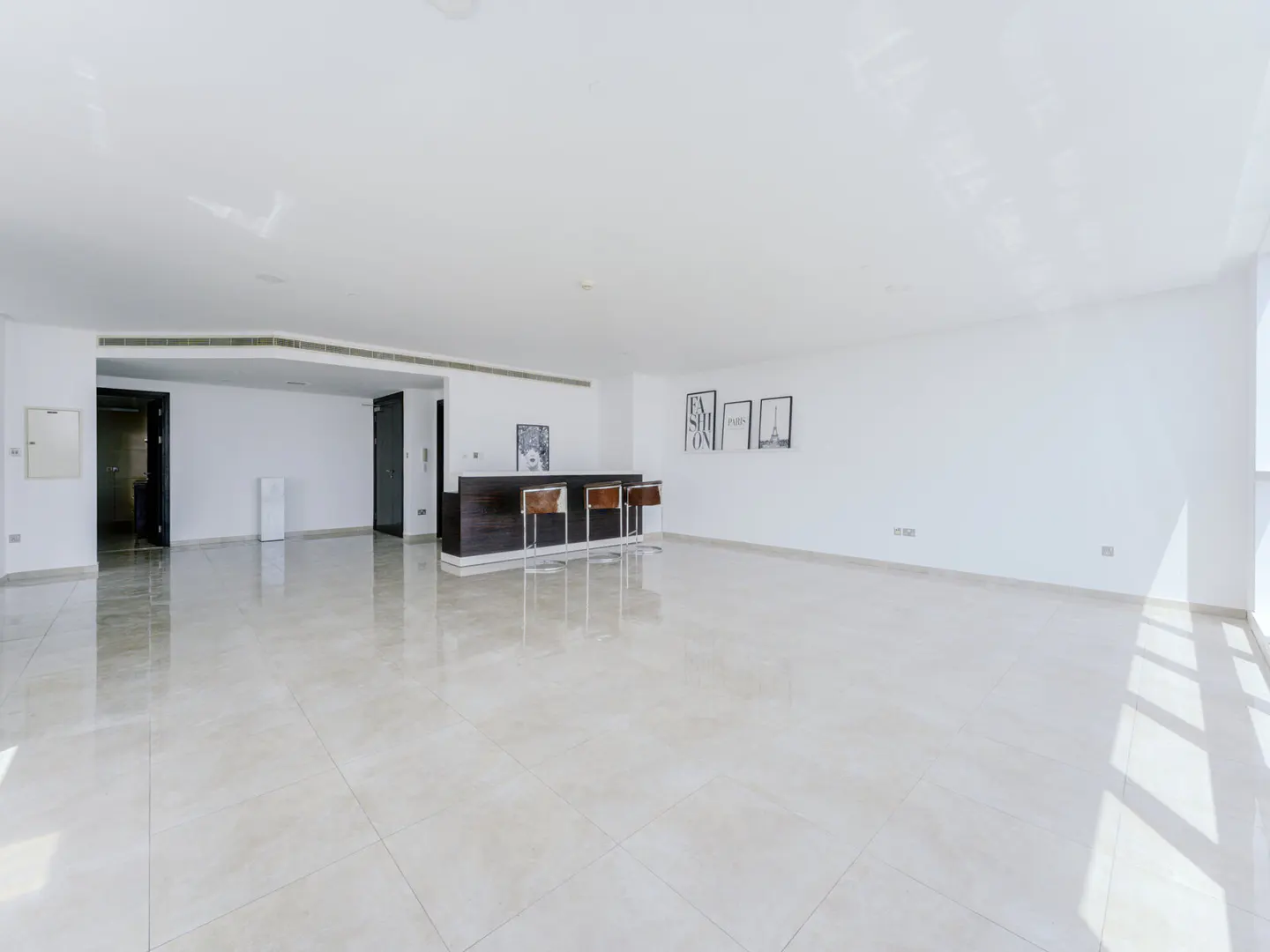 Spacious, bright room with white walls, glossy tiled floors, and a dark bar counter with three stools against the wall.
