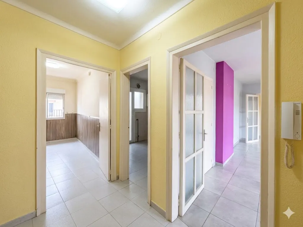 Hallway with yellow walls and white trim. Three open doorways lead to rooms with different colored walls. A white intercom is mounted on the right wall.