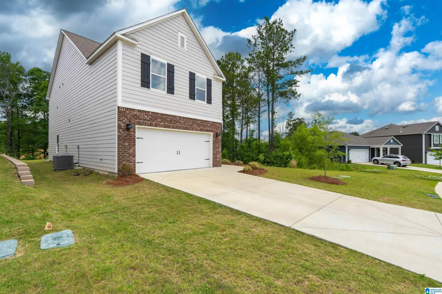 Two-story house with light gray siding, brick accents, and a white two-car garage under a cloudy blue sky.