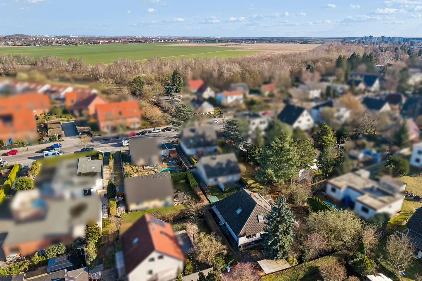 Aerial view of a suburban neighborhood with houses, trees, and a green field in the background.