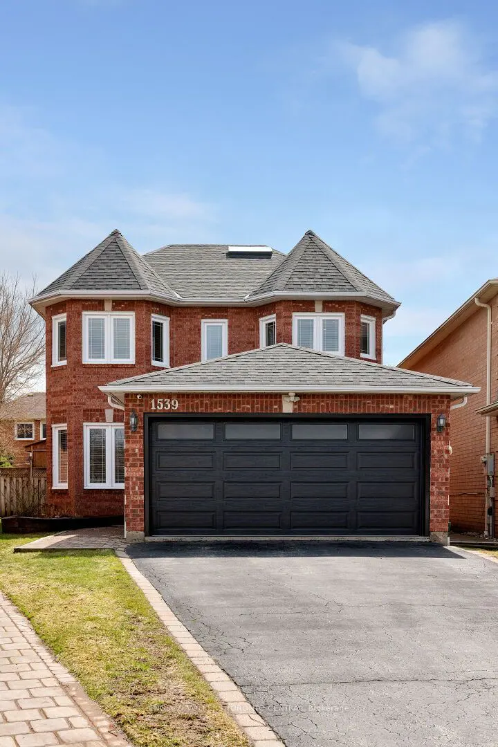 Two-story red brick house with a gray roof and a black three-car garage. The house number "1539" is above the garage.