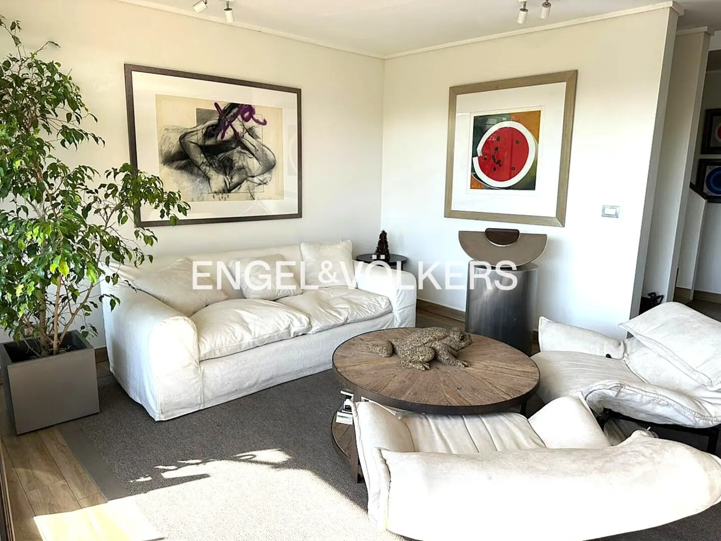 Living room with white sofa and chairs, round wood table with frog statue, and two framed art pieces on the wall.