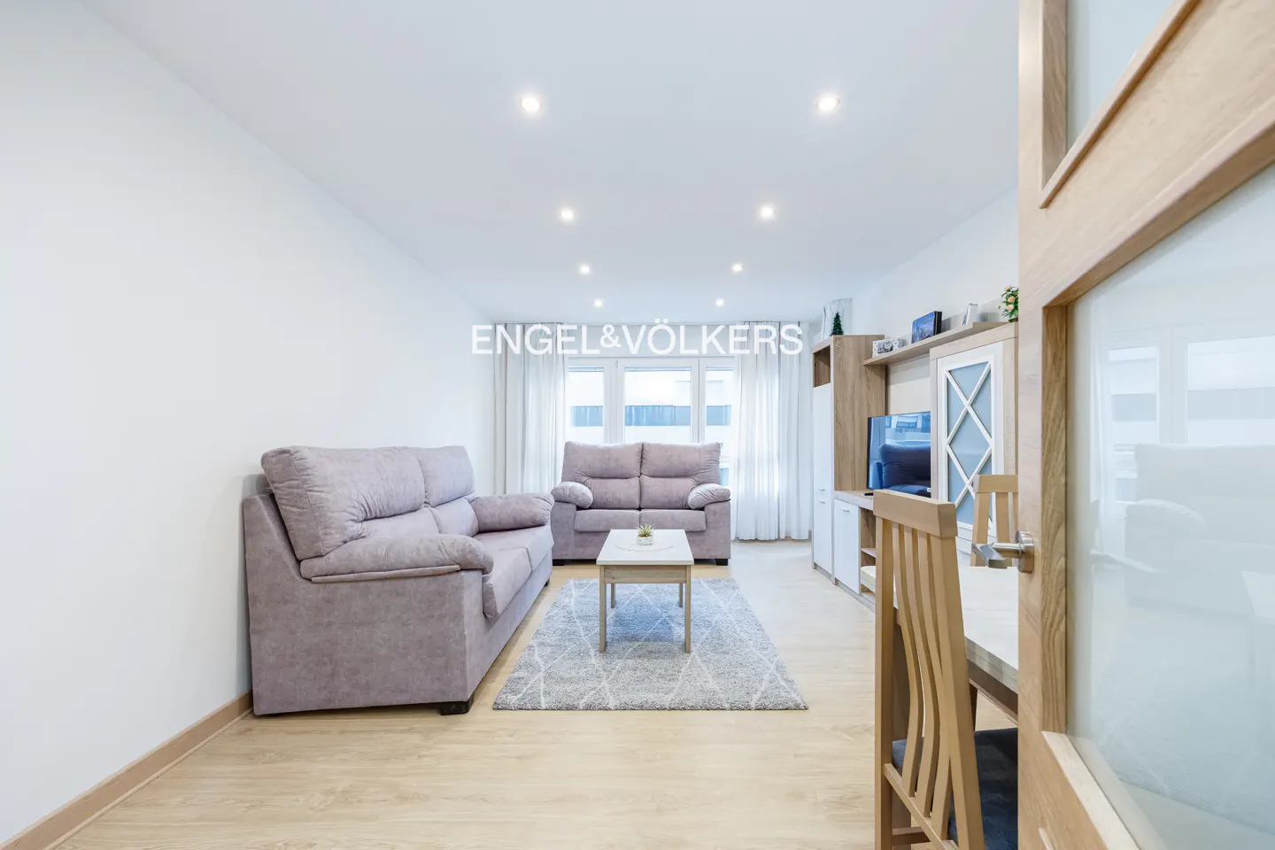Bright living room with light wood floors, two grey sofas, a coffee table on a rug, and a wooden dining set.