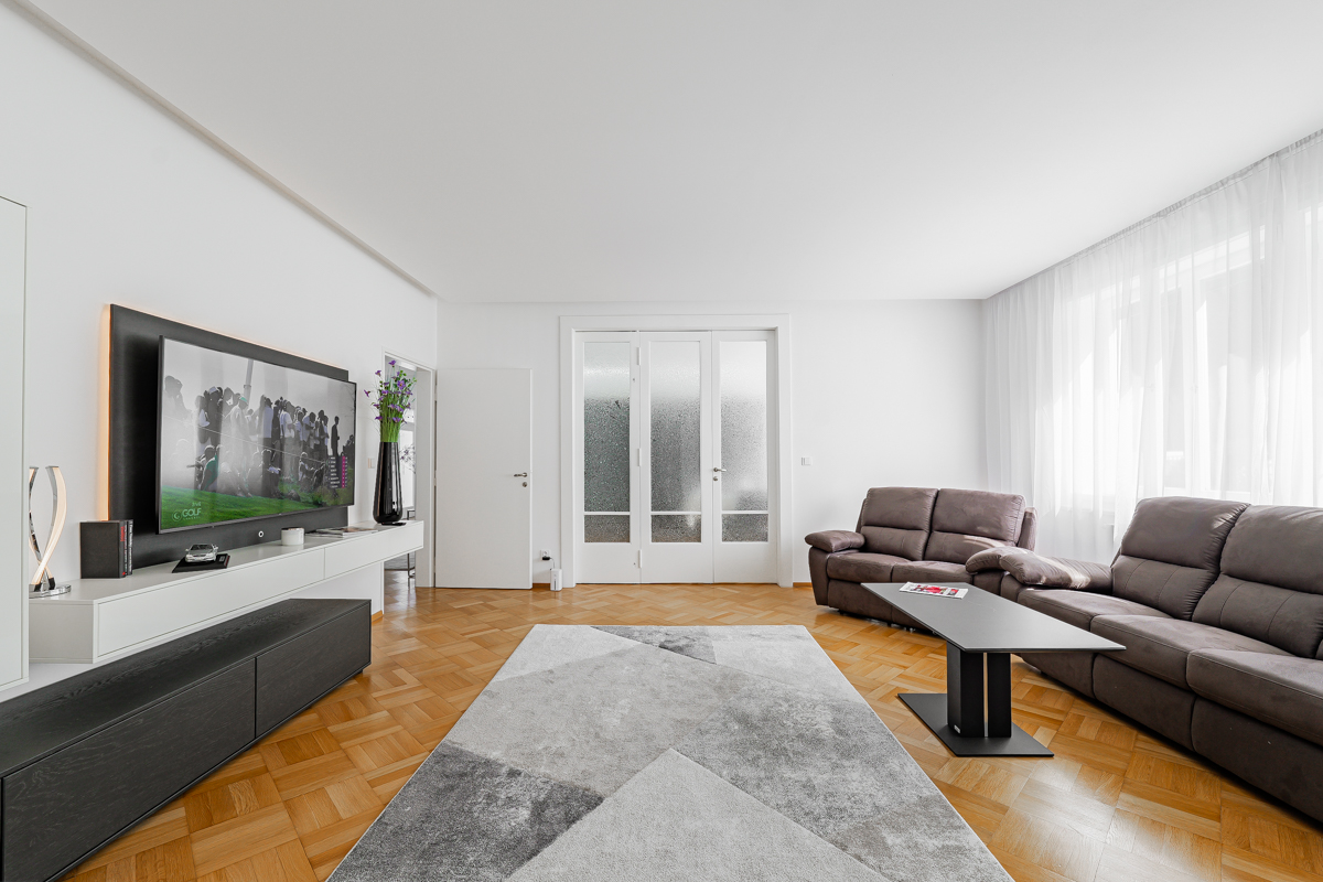 Modern living room with brown leather sofas, a geometric rug, hardwood floors, and a wall-mounted TV on a white console. [AI-generated text]