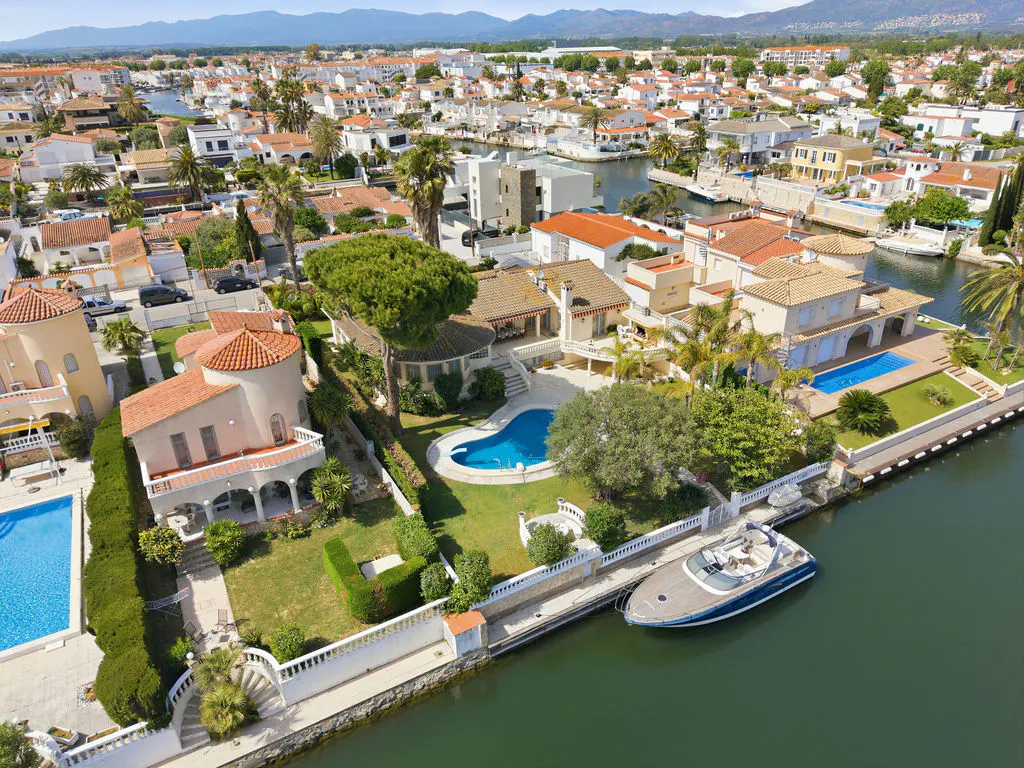 Aerial view of a waterfront community with houses, pools, boats, and canals on a sunny day.