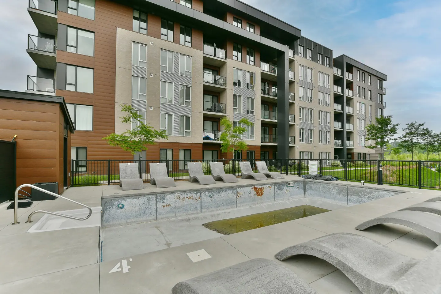 Modern apartment building with a pool deck featuring concrete lounge chairs and a small, empty swimming pool.