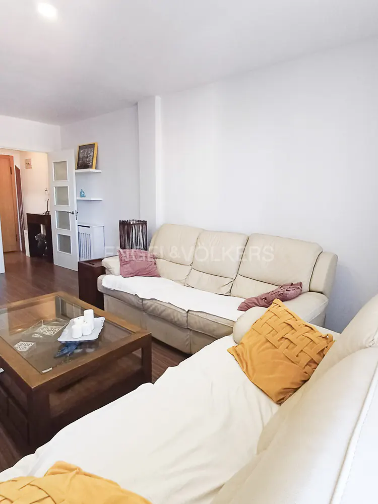 Living room with white walls, wood floors, and beige sofas with orange pillows. A wood coffee table sits in front of the sofa.