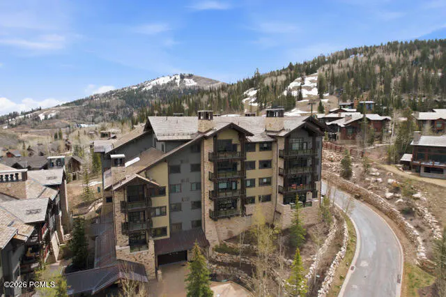 Exterior view of a multi-story condo building with balconies, nestled in a mountain landscape with a winding road.