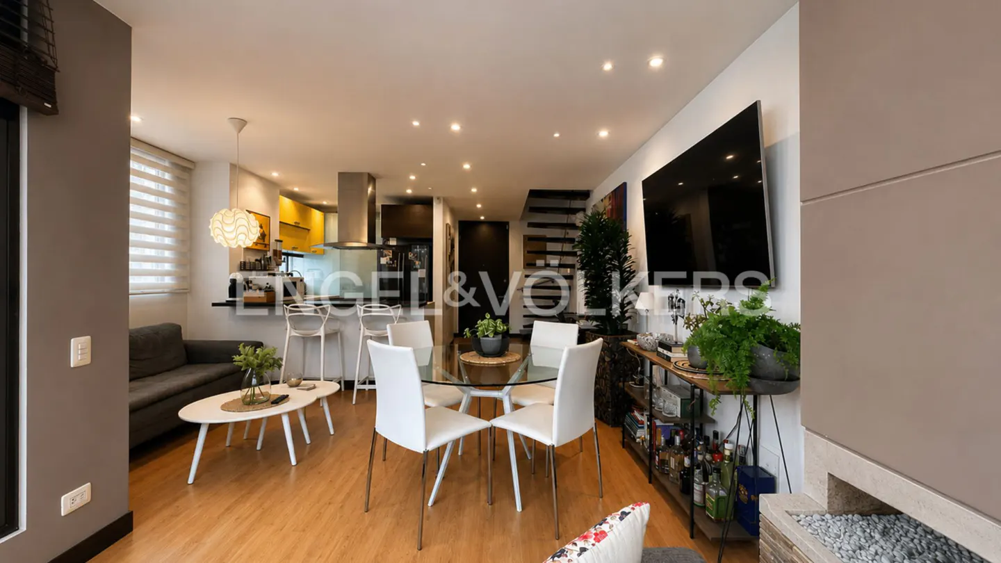 Open-concept living space with wood floors, a glass dining table with white chairs, and a gray sofa. A black kitchen bar is visible.