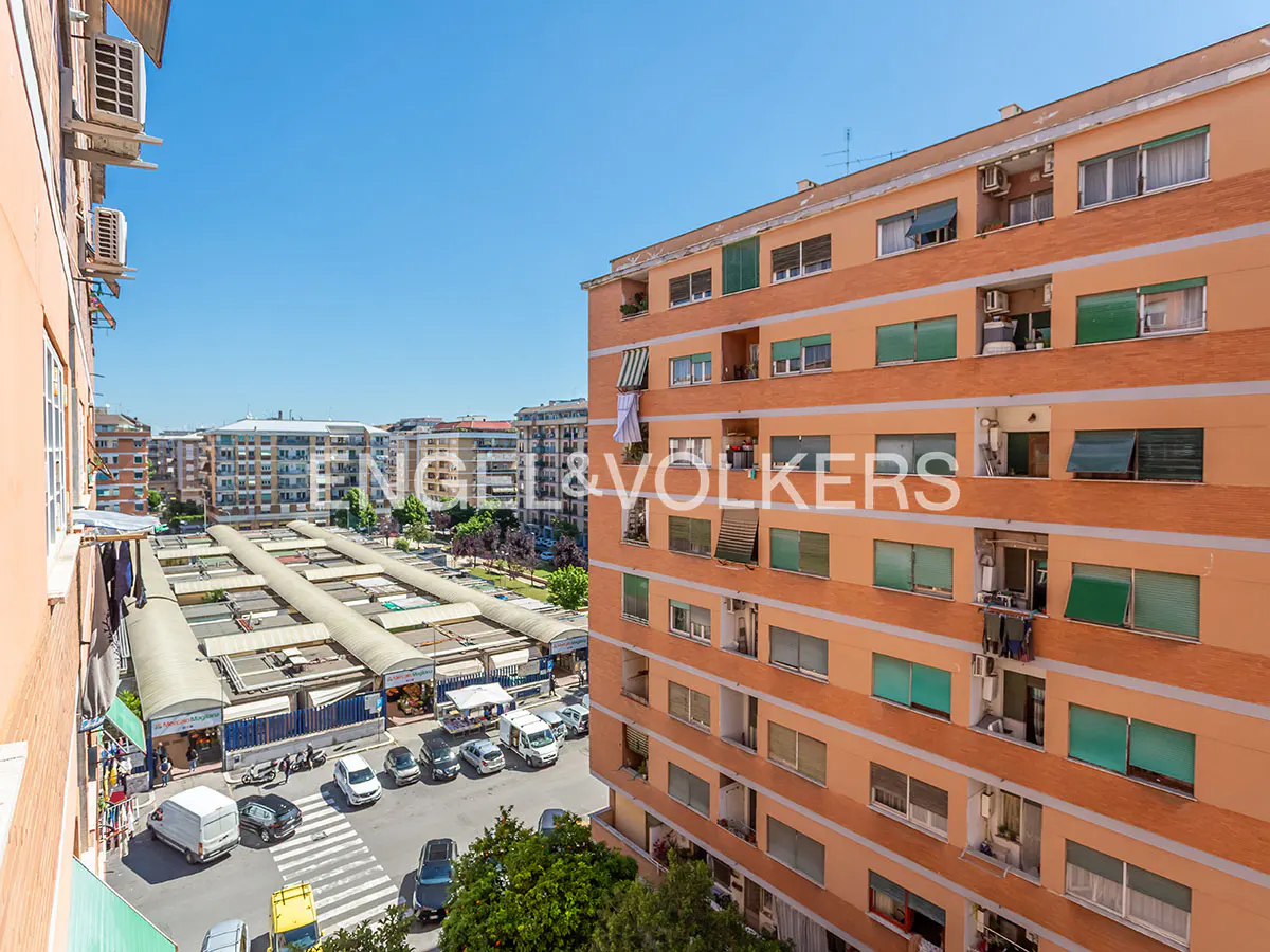 View from a building overlooking a market with white canopies, cars, and other buildings under a blue sky.