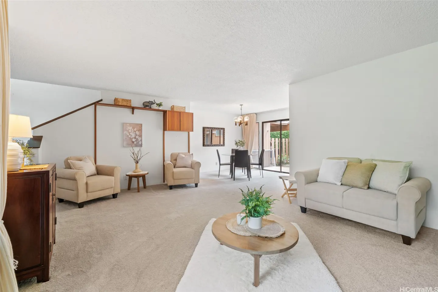 Bright living room with beige carpet, sofa, and armchairs. A dining table is visible in the background.