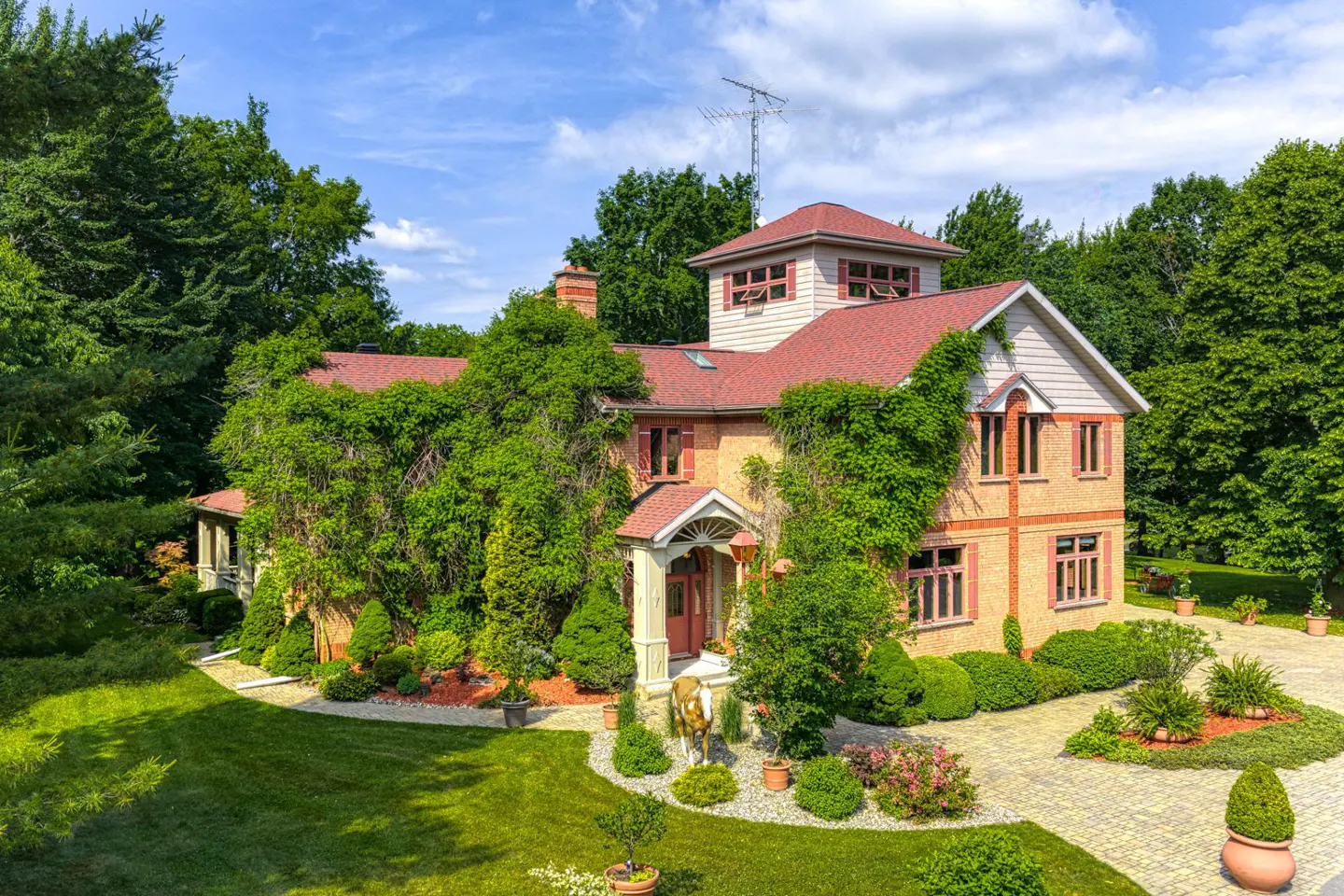 Two-story brick house with a red roof, surrounded by green trees and vines. A statue of a horse stands near the front door.