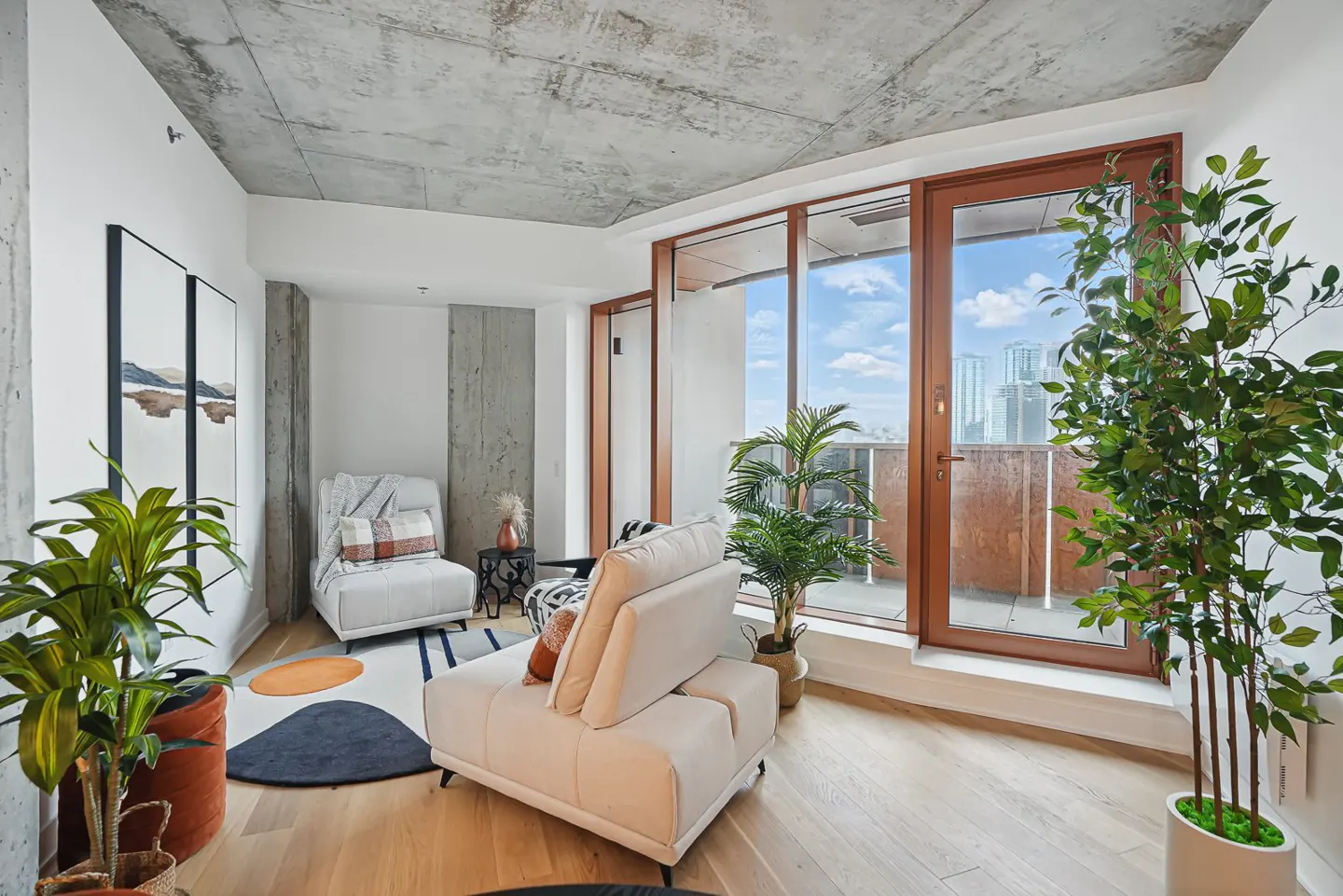Modern living room with concrete ceiling, light wood floors, two white chairs, potted plants, and a balcony view.