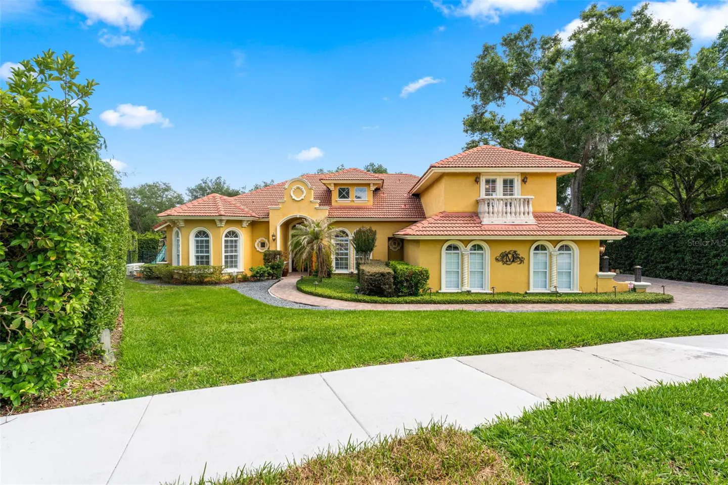 A yellow, two-story house with a red tile roof, white trim, and green lawn under a blue sky.