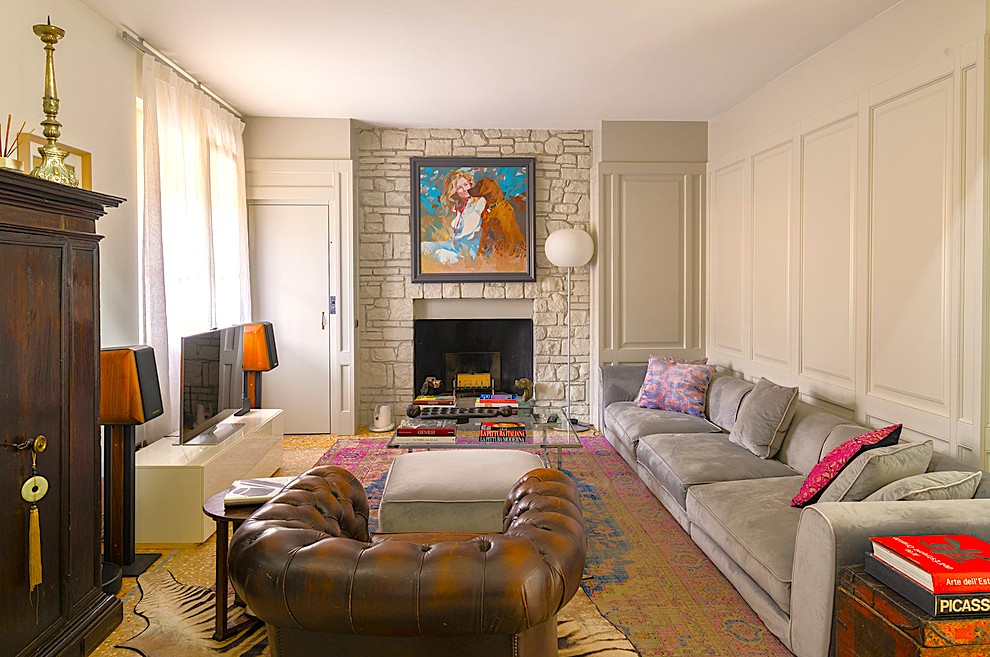 Living room with a stone fireplace, large grey sectional sofa, brown leather armchair, and a colorful patterned area rug. [AI-generated text]