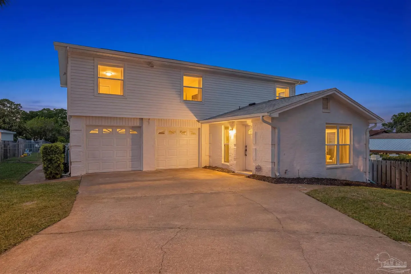 Two-story white house with a two-car garage and a concrete driveway at dusk. Lights are on inside.