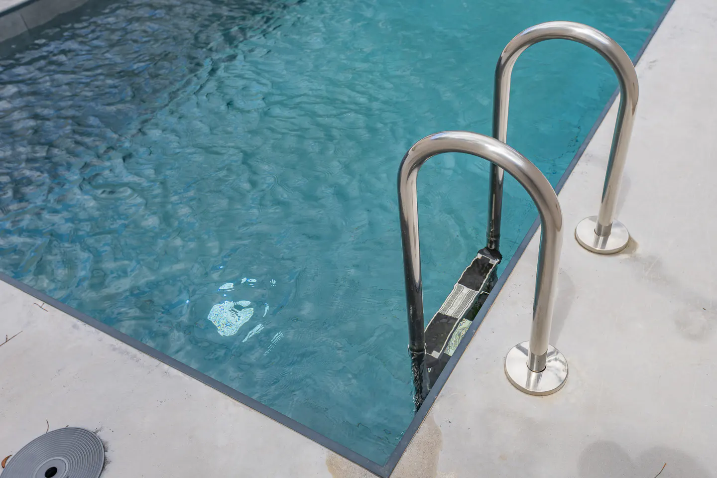 A swimming pool with clear blue water and a stainless steel ladder for easy access.