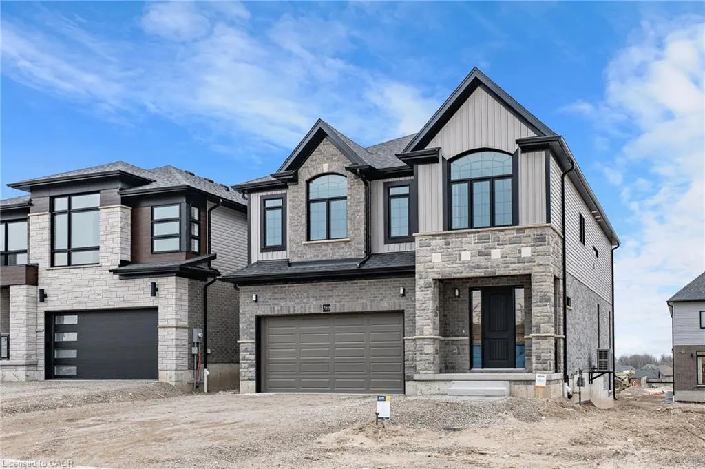 Two-story house with gray stone and siding, black trim, and a gray garage door under a cloudy blue sky.
