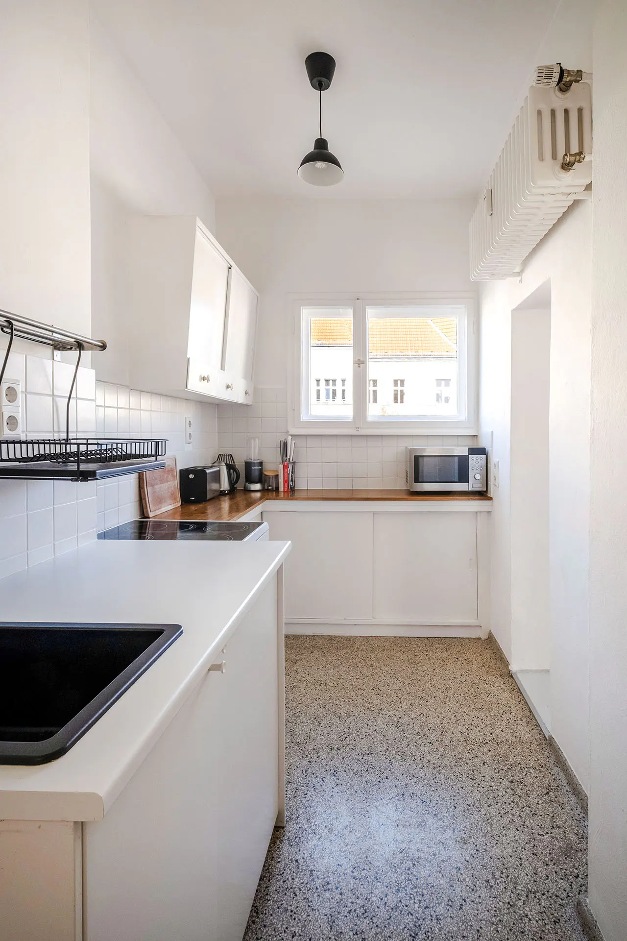 Bright, white kitchen with speckled floor. Black sink in island, white cabinets, and window with view of building.