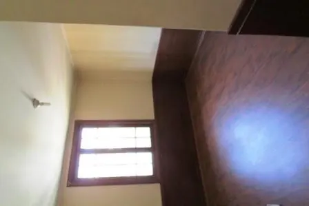 A bright room with a window, light walls, and a dark wood floor. A ceiling fan is visible.